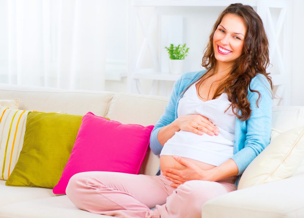 Pregnant Happy smiling Woman sitting on a sofa and caressing her