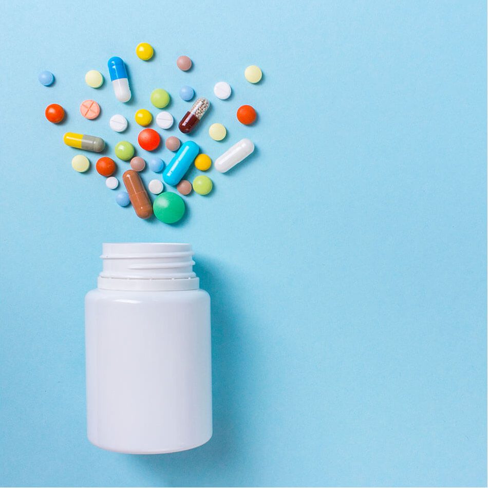 Various of pills of different shapes and sizes spread out above a white pill container