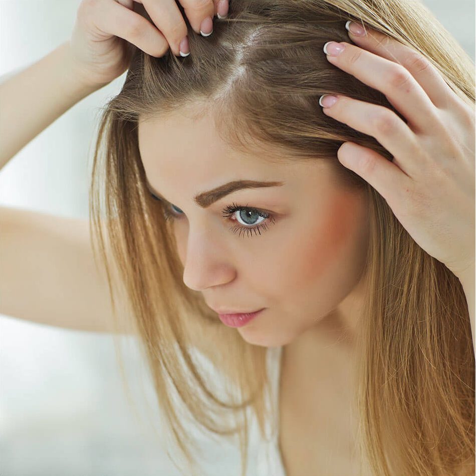 Woman spreading her sandy blonde hair at her hair line checking for hair loss