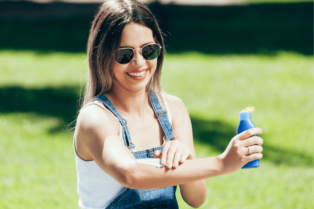 woman with sunglasses outdoors applying sunscreen