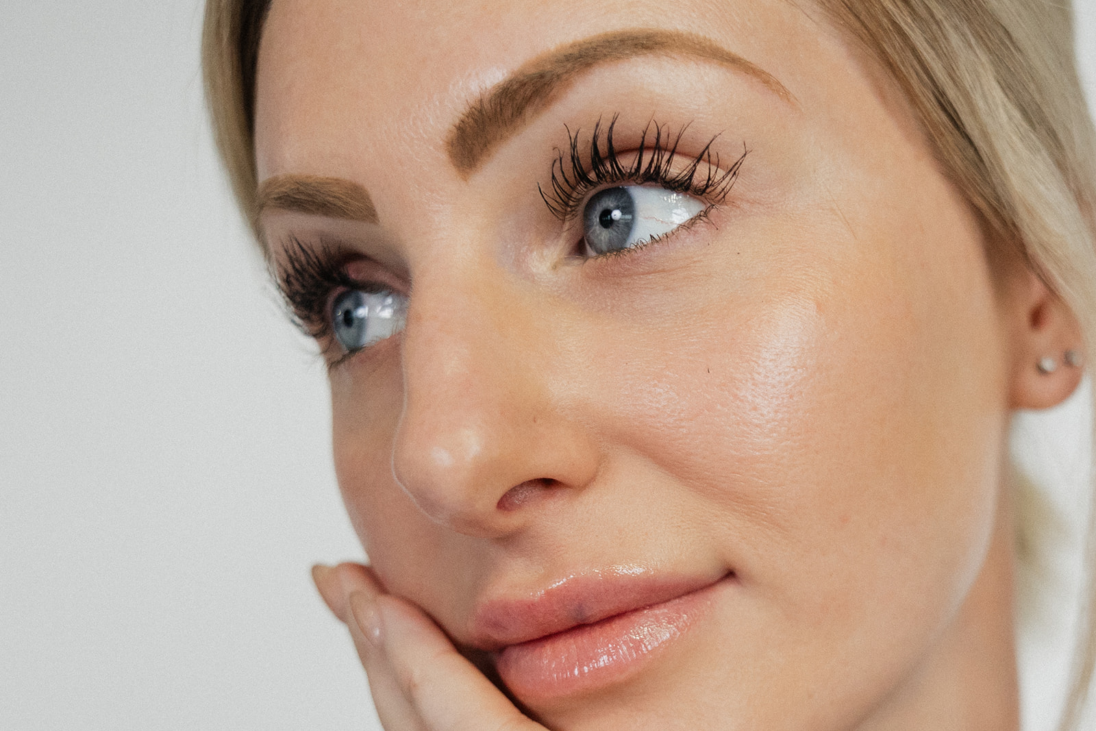 Woman with long eyelashes and gray blue eyes touching her face with her hand