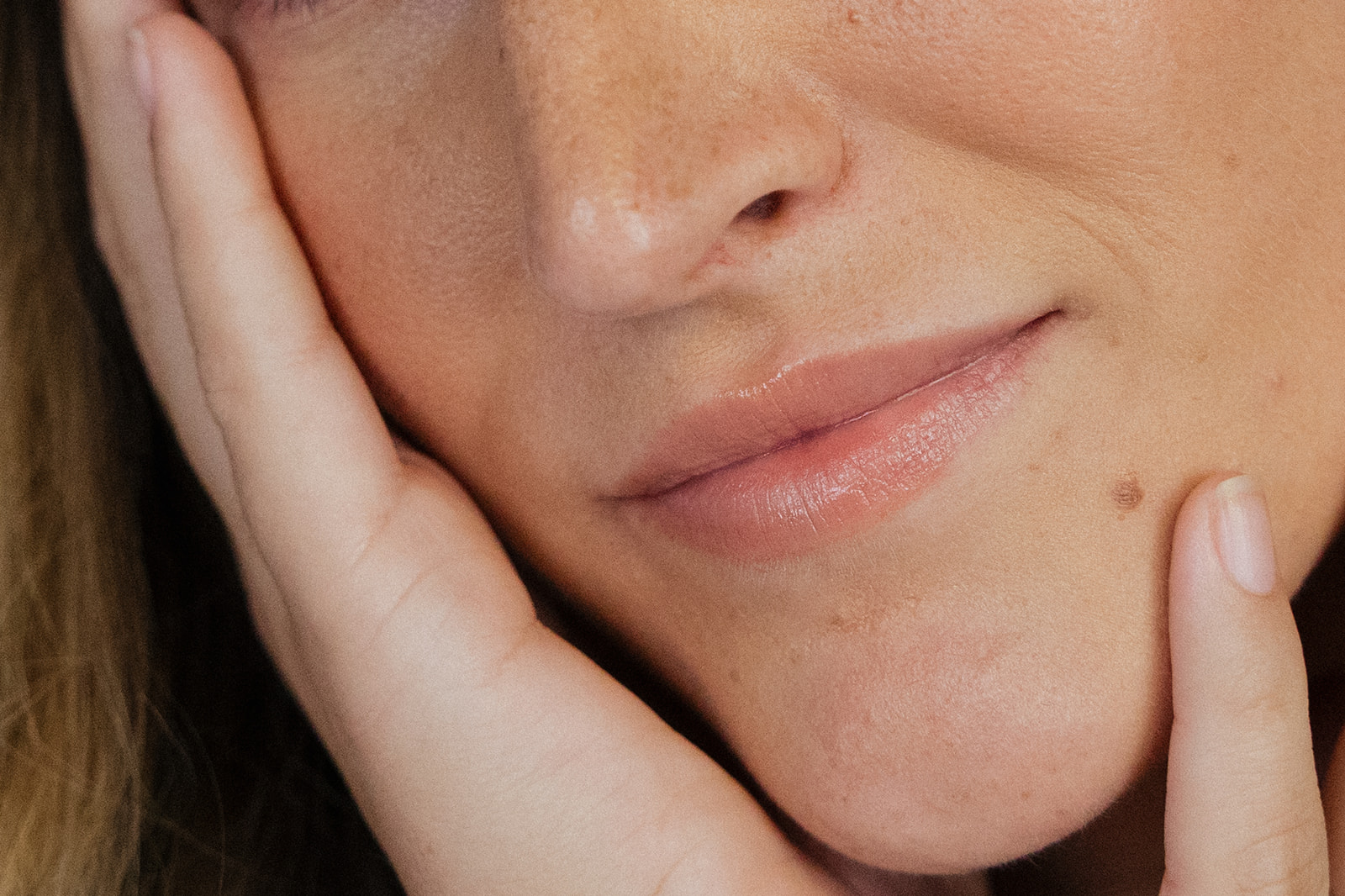 Close up of a woman's face showing nose and lips with hand holding side of face