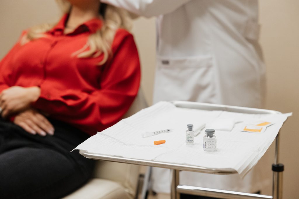 Patient lying on recliner chair getting fillers, the filler solution with glass jar on a chair and syringe laying next to them.